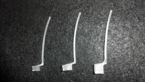 Three small, clear Concha Lock devices with a bent, elongated shape are arranged side by side on a dark textured surface.